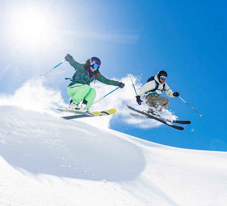 Two skiers jumping on snowy slope.