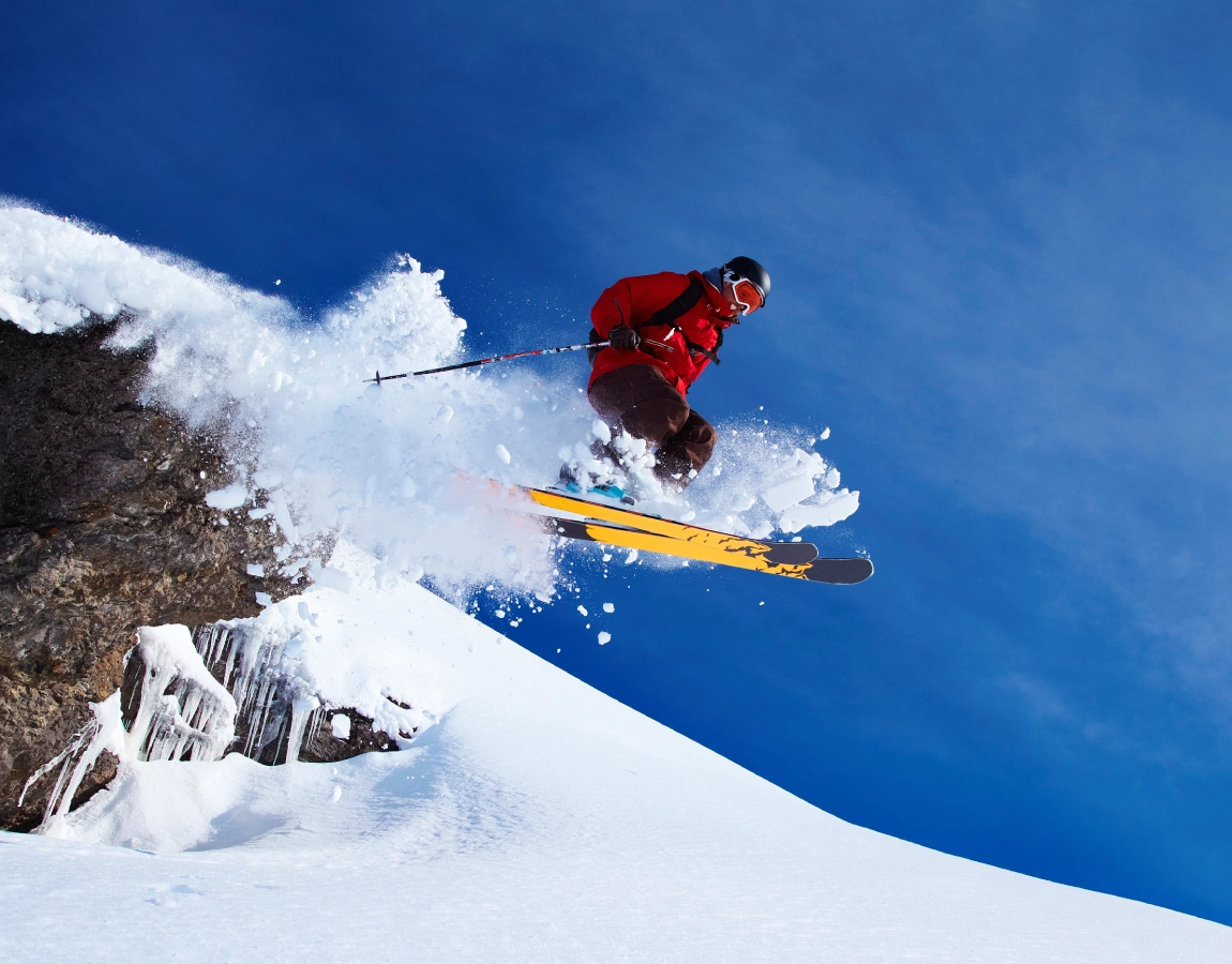 Skier jumping off snowy mountain cliff.