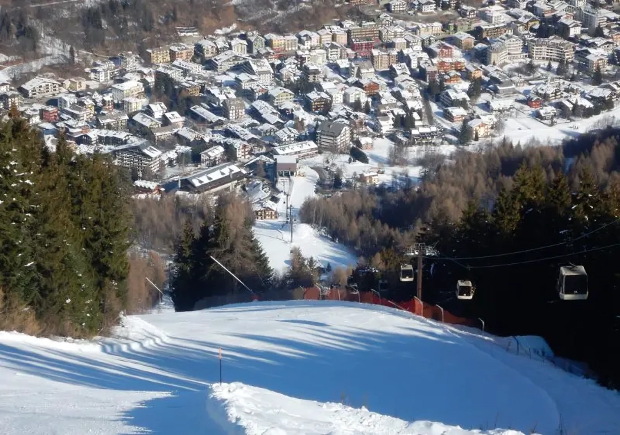 Snowy ski slope with town and gondolas.