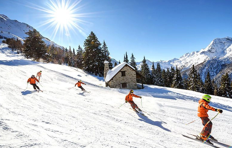 Skiers descending snowy mountain under bright sun.