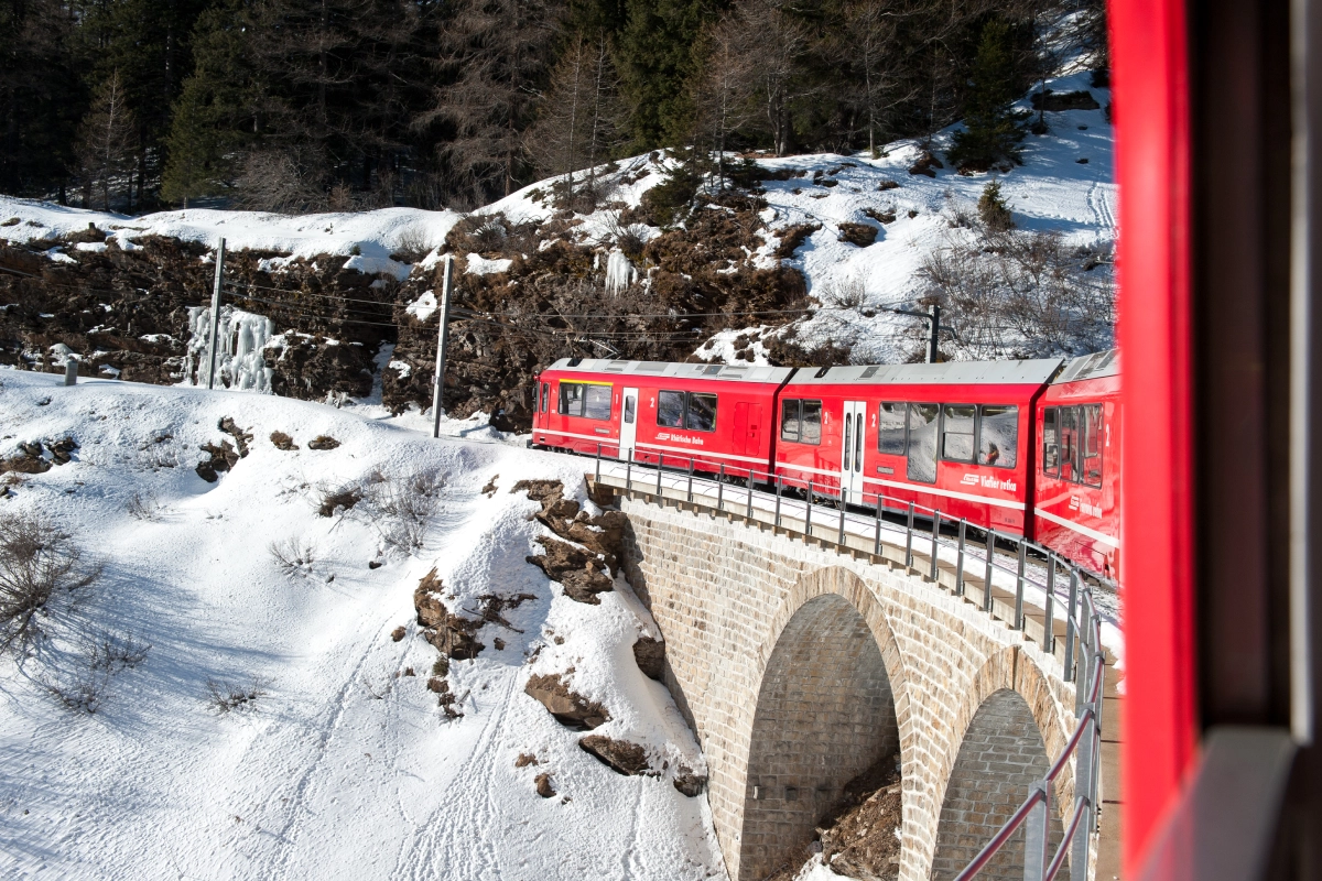 Red train on snowy mountain bridge.