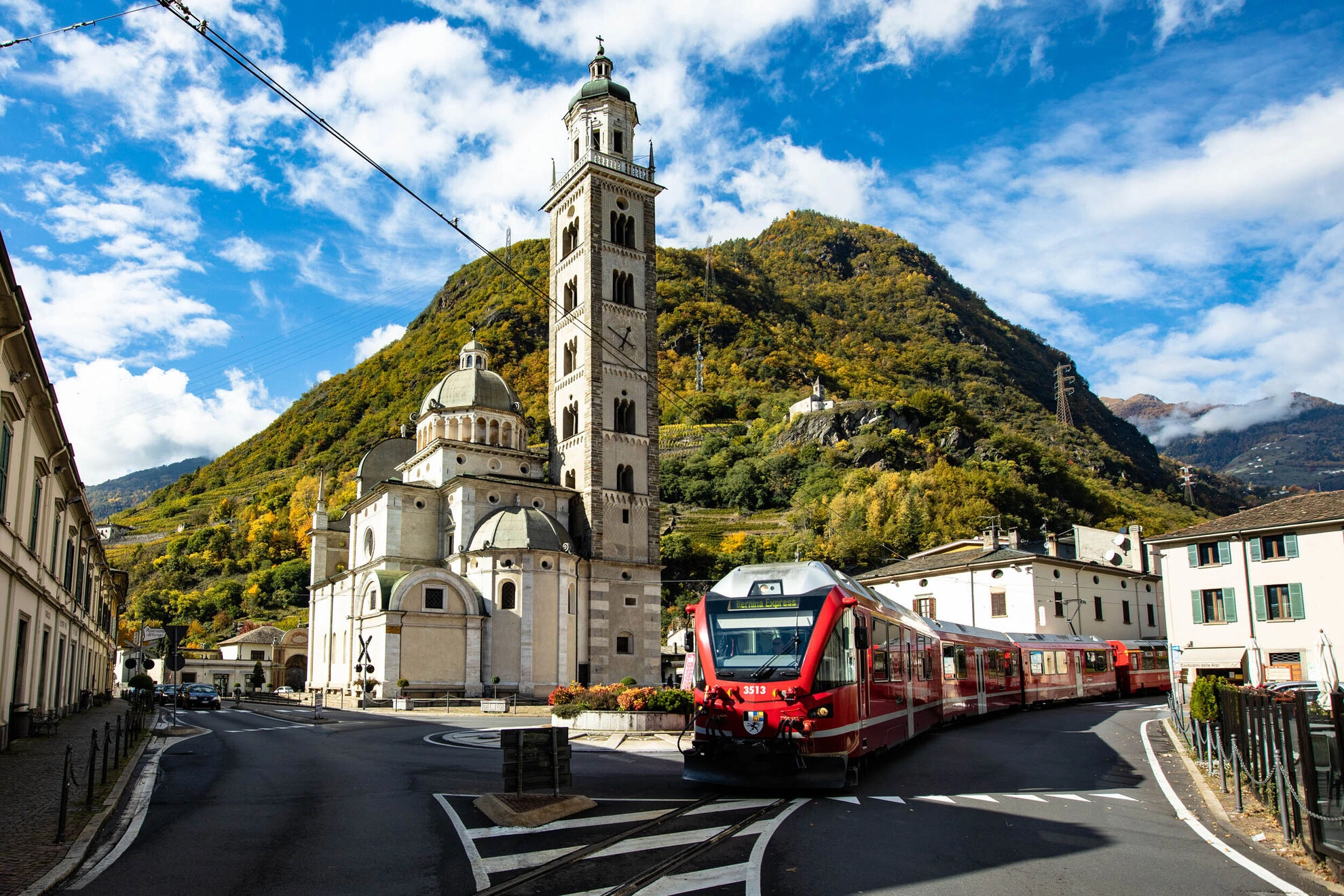 Train passing by church and mountain scenery.