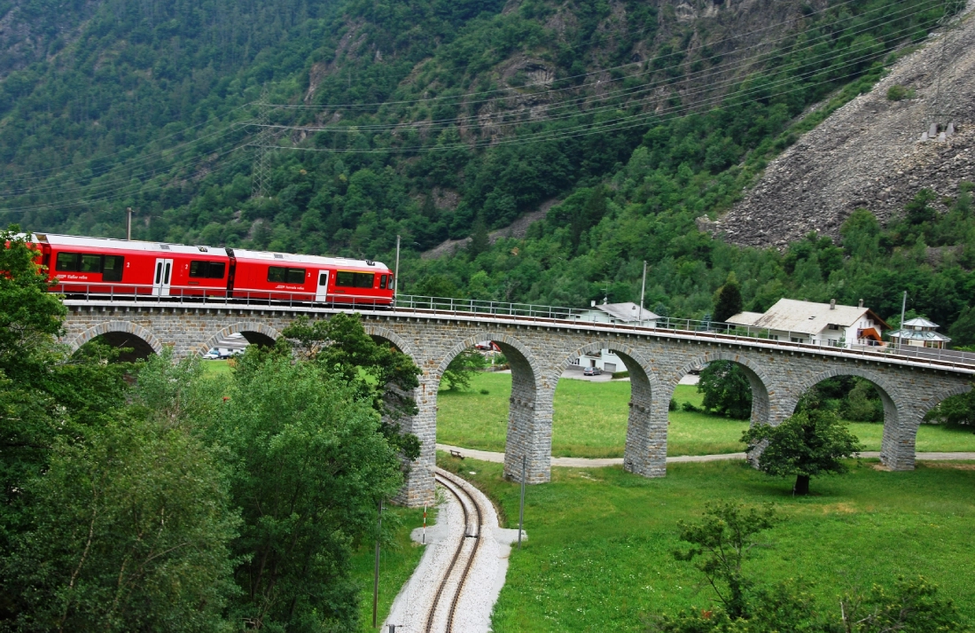 Red train crossing a stone bridge.