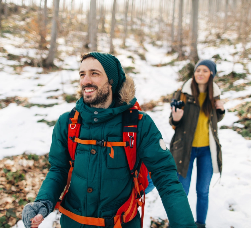 Smiling hikers walking through snowy forest trail.